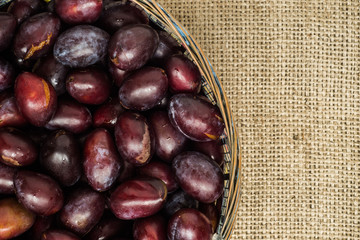 Fresh prune plums in basket on canvas background..