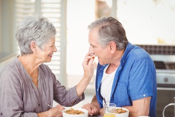 Side view of senior woman feeding husband while sitting at table
