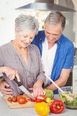 Senior woman cutting while man embracing in kitchen