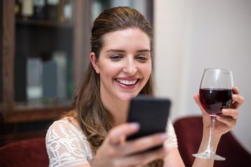 Cheerful woman holding wine glass while using phone