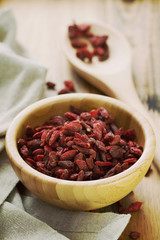 berries goji in bowl with spoon on brown wooden background