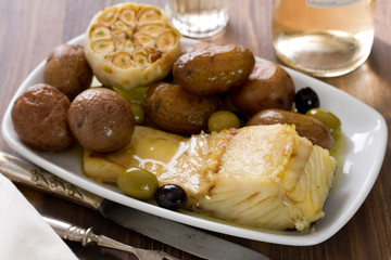 fish with potato and olives on white dish on brown wooden background