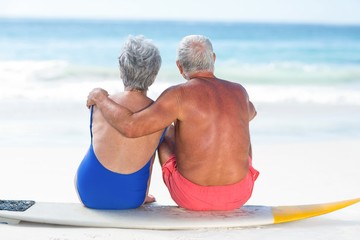 Cute mature couple sitting on a surfboard