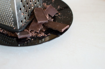 Grater and grated chocolate on a wooden table.