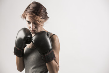 Donna Boxer sta in posizione di guardia con i guanti neri e la canotta grigia su fondo bianco