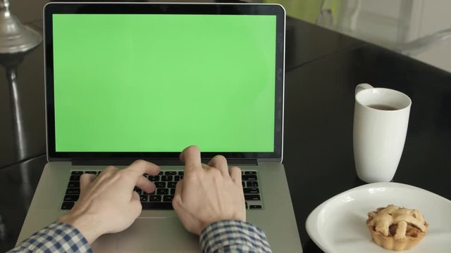 A man types on a laptop on his desk.  Green screen for your custom screen content.
