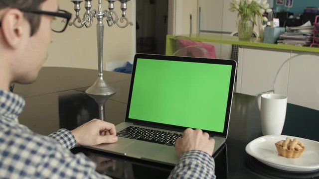 A man types on a laptop on his desk.  Green screen for your custom screen content.