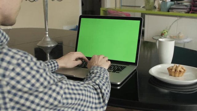 A man types on a laptop on his desk.  Green screen for your custom screen content.