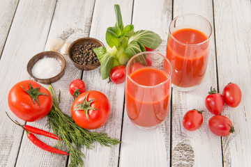 Glass of tomato juice with vegetables on old wooden background, with greenery and tomatoes