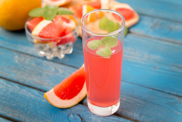 Freshly squeezed orange and grapefruit juice in glass, with fruits on wooden background