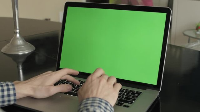 A man types on a laptop on his desk.  Green screen for your custom screen content.