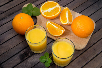 Freshly squeezed orange juice in glass, with fruits on wooden background