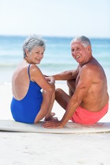 Cute mature couple sitting on a surfboard