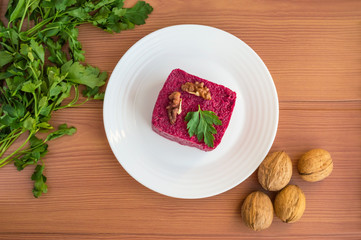 Vitamin salad of boiled beets in the form of a square, with walnuts on a white plate