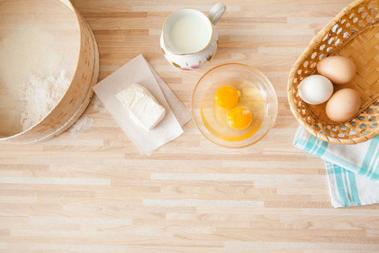 Ingredients for bread baking on light wooden background  with copyspace. Eggs in braided bucket, flour, raw eggs, milk, butter, towel, sieve. Cuisine background.