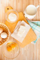 Fototapeta na wymiar Ingredients for bread baking on light wooden table. Butter and salt on cutting board and towel, eggs, raw eggs, milk.