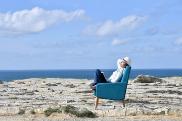 Woman in armchair relaxing on a cliff by the sea