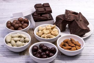 Chocolate, candies, raisins, nuts in the separate bowls on a grey wooden board