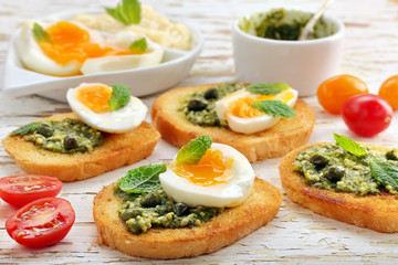 Fresh toasts with pesto and egg on wooden background