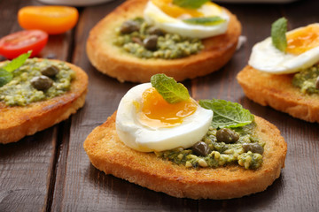 Fresh toasts with pesto and egg on wooden background