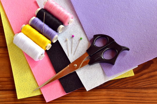 Felt sheets, scissors, thread, needle, pins on a brown wooden background