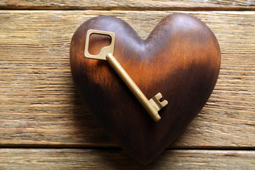 Golden key with brown heart on wooden background