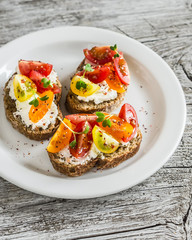 Tomato and cheese bruschetta on a white plate on rustic light wooden board. Healthy breakfast, snack or appetizer with wine