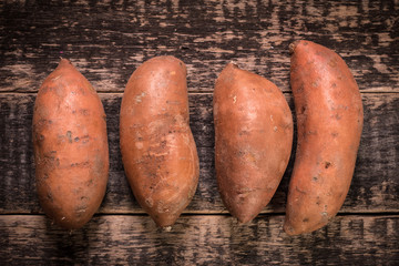 Raw sweet potatoes on wooden background closeup