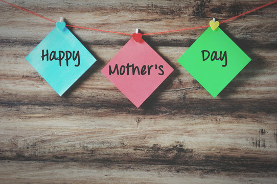 Happy mother's day on colorful paper with clothespin hanging on a string with wooden background, retro style.
