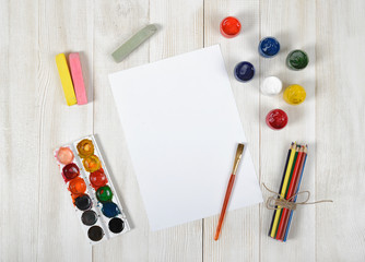 Work place of designer with colored pencils, brush, gouache jars, watercolor paints, chalks and a...