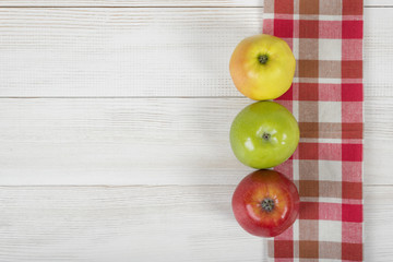 Three apples placed on red checkered kitchen tablecloth. Top view.