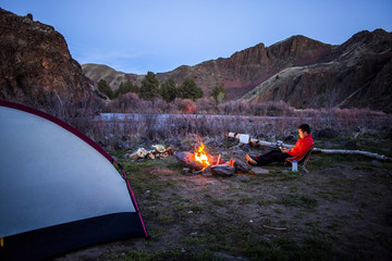 Caucasian hiker sitting near campfire in desert field, Painted Hills, Oregon, United States