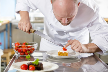 Obraz na płótnie Canvas Professional chef decorates dessert cake with strawberry in kitchen