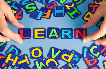 Word Learn spell out on blue table with woman hands and letters. Letters drawn by me.