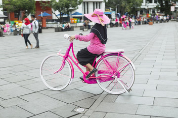 Young woman in pink hat riding a bicycle in city. Active people. Outdoors