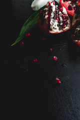 Delicious pomegranate fruit and lilies on black background. Stil