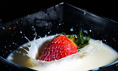 Red fresh strawberry falling with a juicy splash from a height in a bowl filled with white milk 