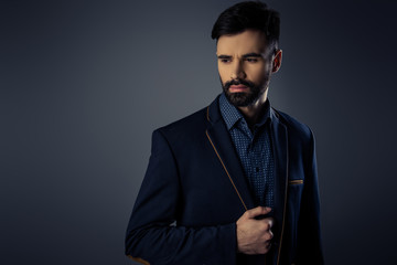 Obraz premium Portrait of stylish businessman touching jacket on gray backgro