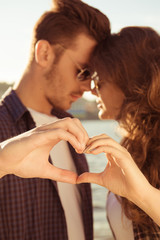 Fototapeta premium Romantic couple in love gesturing a heart with fingers at sunset