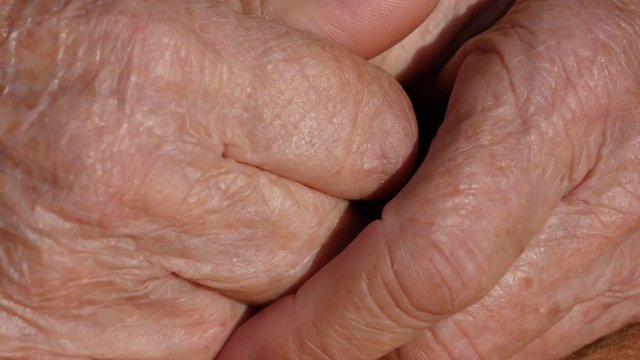 Senior woman massages painful hands . Wrinkled skin on the fingers of grandmother close-up