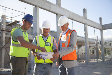 Architects reading blueprints while standing at construction site