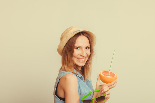 Happy woman in hat holds sunglasses and grapefruit