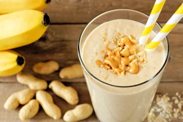 Photo sur Plexiglas Milk-shake Peanut butter banana oat smoothie with paper straws on rustic table with scattered ingredients