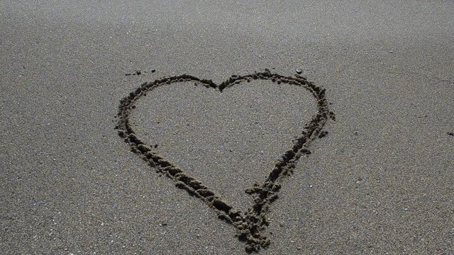 Wave washes over heart in the sand. Love and heart break concept.