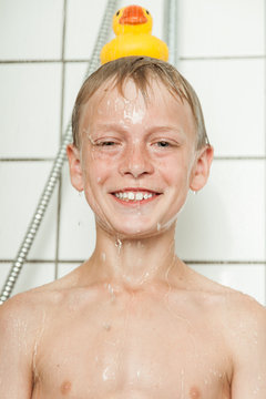 One boy smiles under running shower by tiled wall