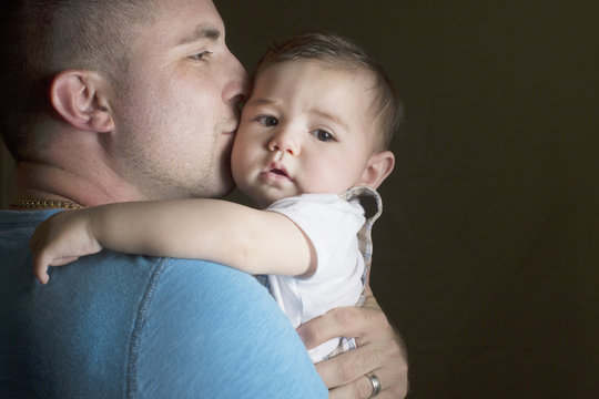 Father kissing his cute baby boy against black background