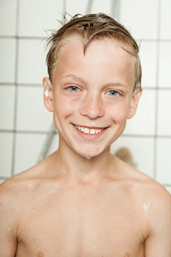Blond wet smiling boy stands in tiled bathroom
