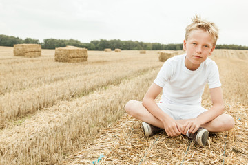 Naklejka na ściany i meble Boy sits alone in harvested wheat field