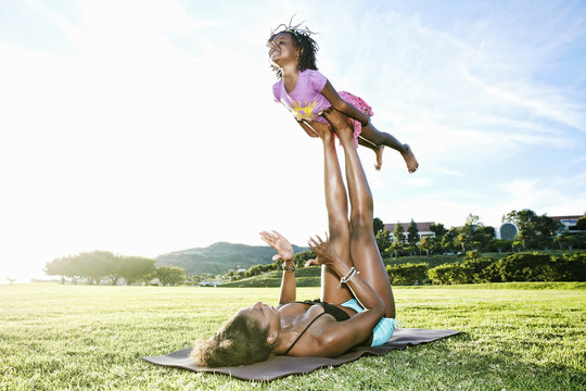 Mother holding daughter with legs on yoga mat in park