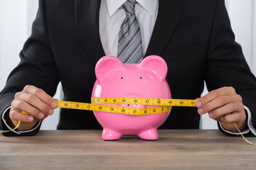 Businessman Measuring Piggybank On Desk